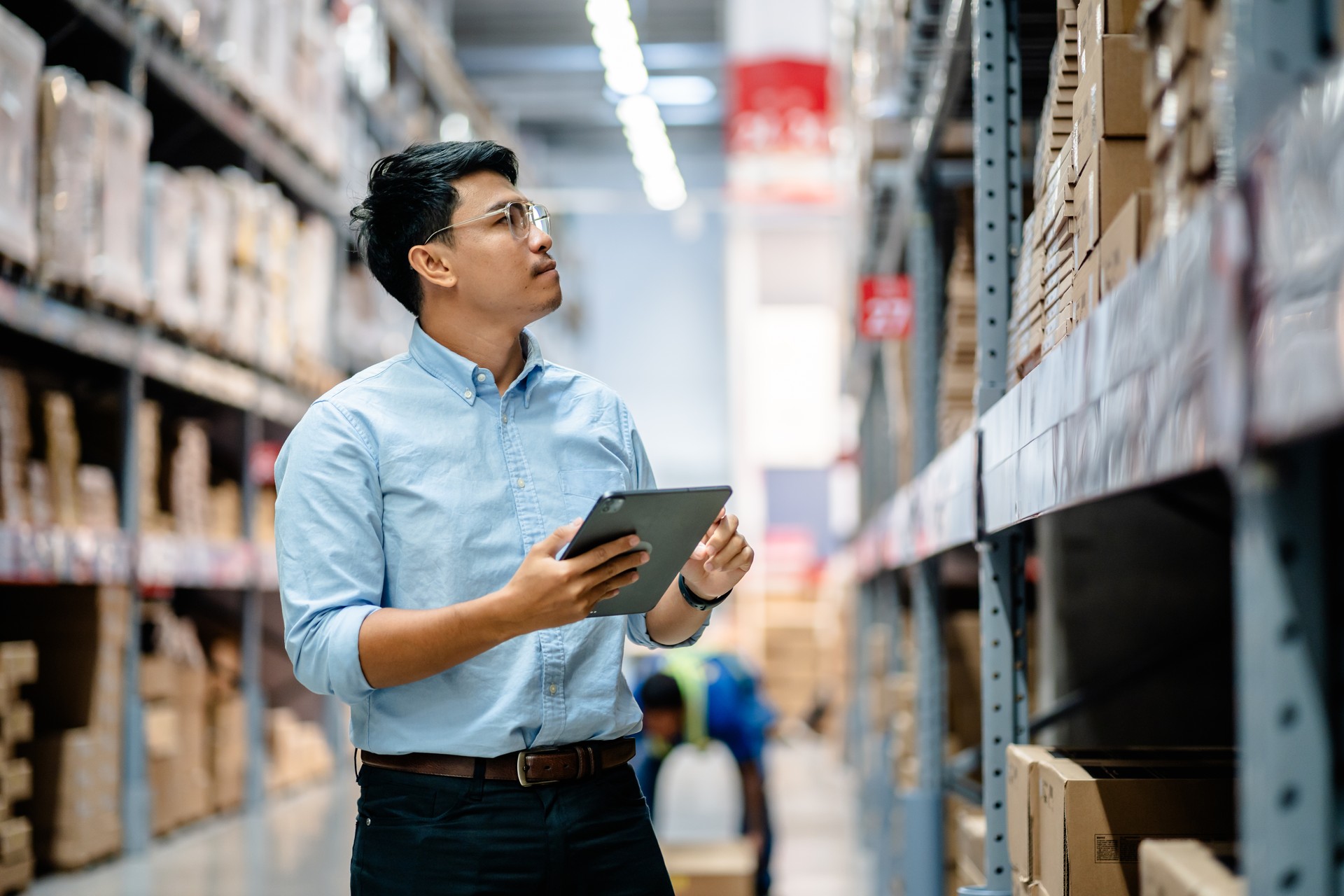 Businessmen or manager use a digital tablet to check the stock inventory on shelves in large warehouses, a Smart warehouse management system, supply chain and logistic network technology concept.